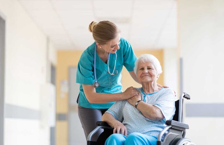 Adult daughter sitting next to elderly mother on a couch, having a caring conversation and holding hands