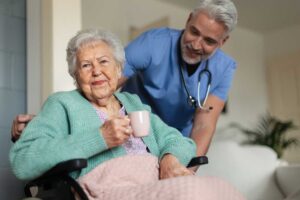 Older adult arranging framed photos and clothing in a bright assisted living room with family nearby.