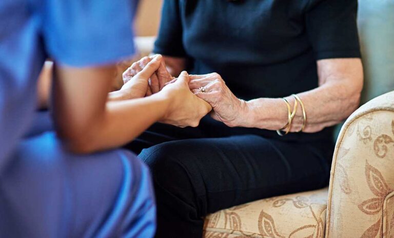 Family members sit beside an older adult in a warmly lit assisted living room, reviewing care documents together.